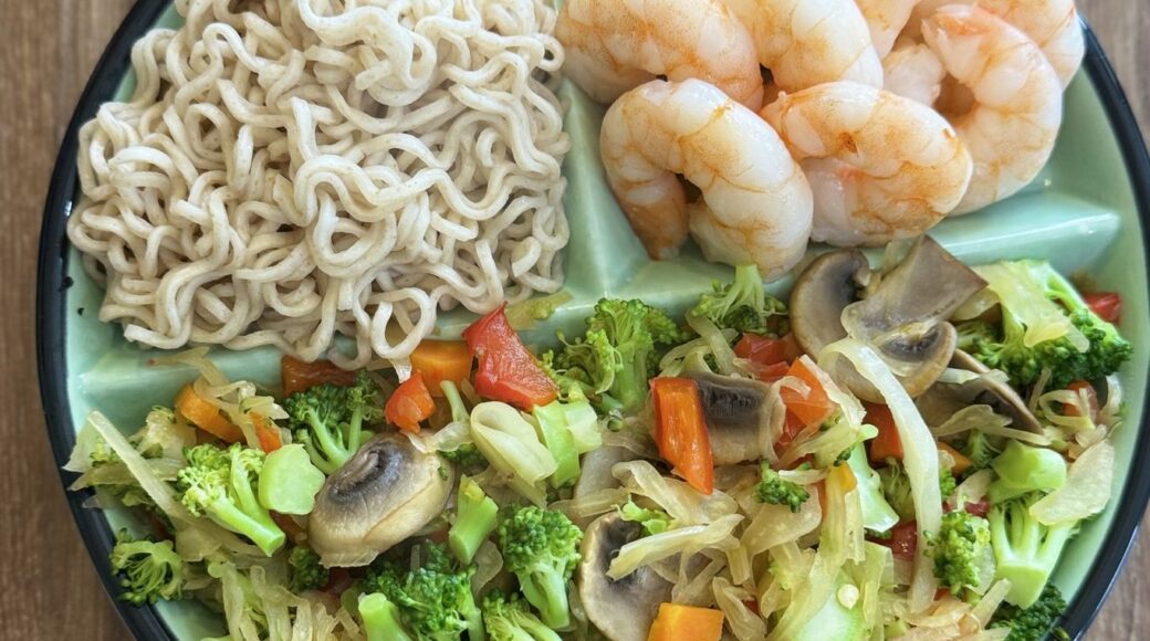 Shrimp, noodles and stir-fried vegetables portioned on a healthy eating plate